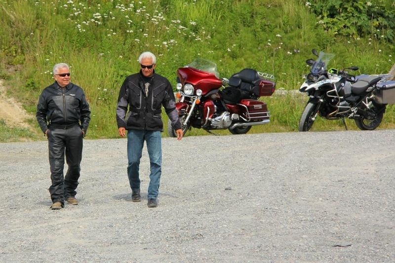 Two old motorcycle riders walking away from their motorcycles.
